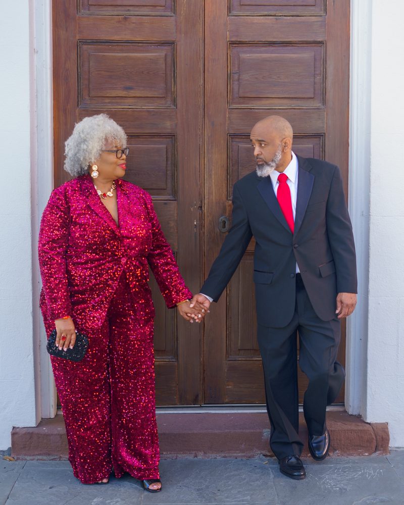 Anniversary couple holding hands in front of a historic carved wooden doorway in downtown Charleston