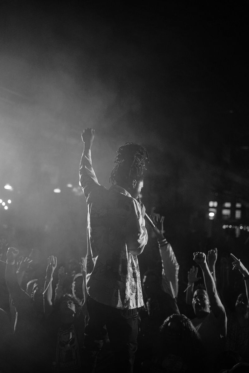 Fan raising a fist in the haze and stage light during GZA's Charleston show, black and white concert photography