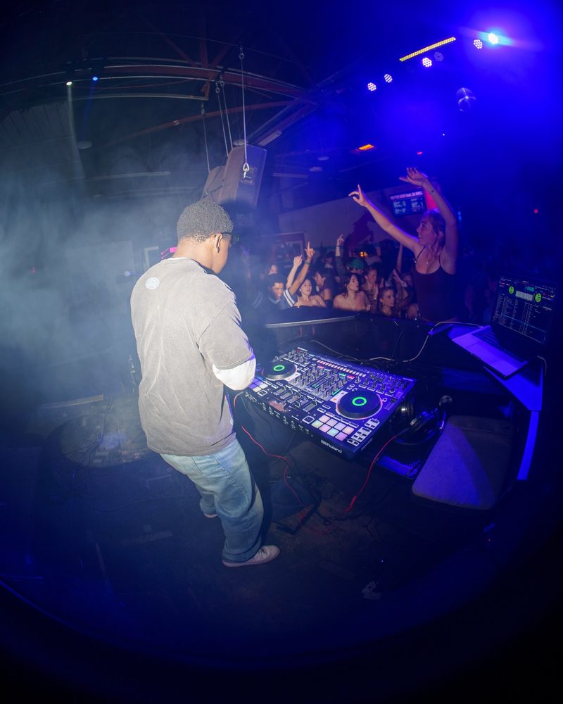 DJ behind the decks with the crowd visible under blue and purple stage lights