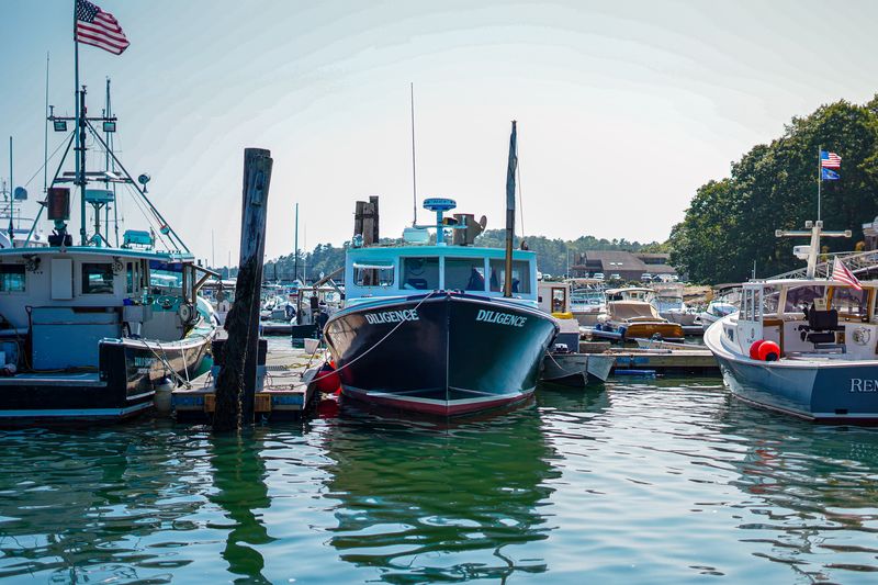 Lobster boat named Diligence docked in a busy Maine harbor with an American flag flying