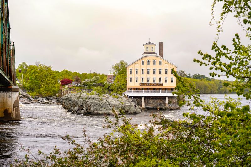 Old mill building turned brewery perched over river falls in Maine, shot from a bridge on an overcast day