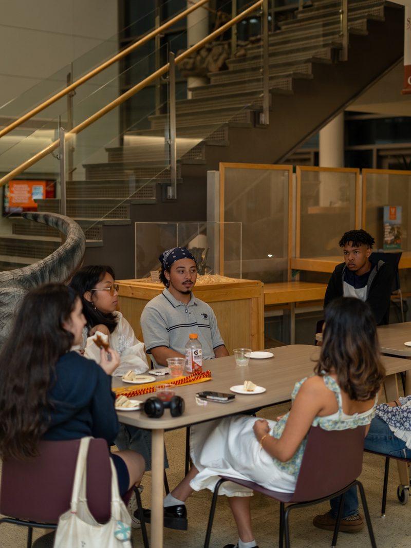 Students seated around a table under mixed fluorescent and warm indoor lighting at a graduation night