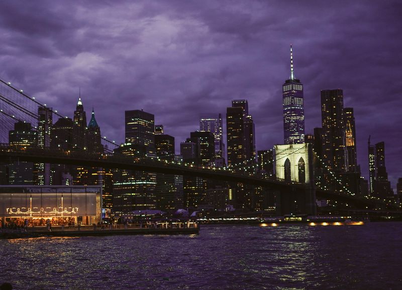 Manhattan Bridge tower lit against a purple dusk sky with One Manhattan Square tower in the background