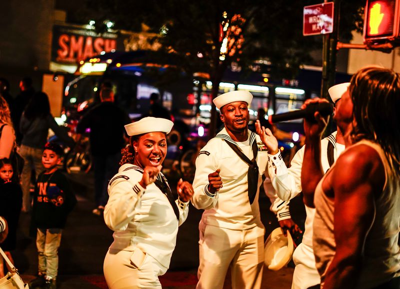 Sailors in dress whites dancing on a New York City sidewalk during Fleet Week at night