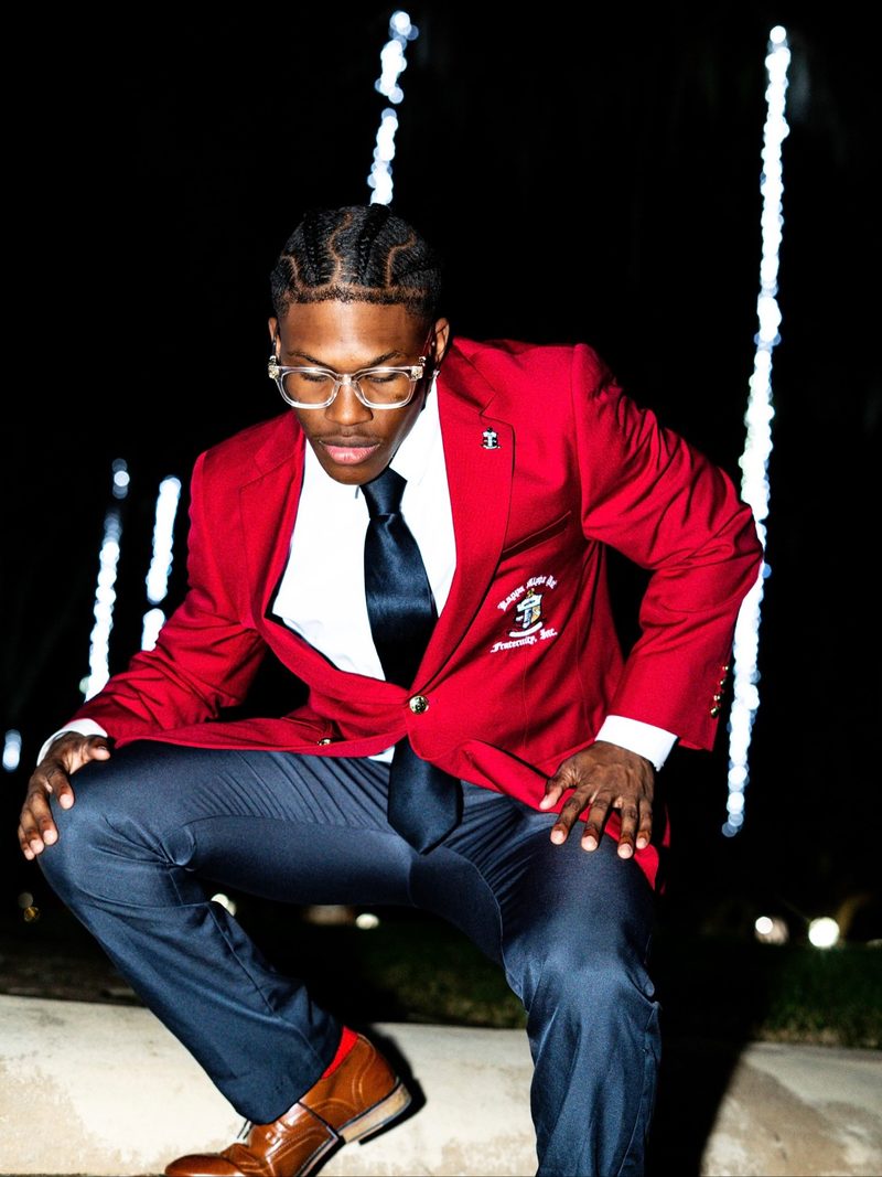 Kappa Alpha Psi member in red blazer with string lights bleeding into the background from a dragged shutter