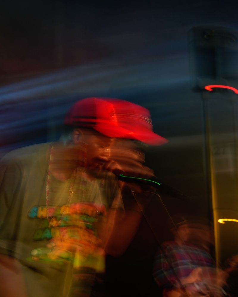 Shutter drag portrait with camera twist creating light trails around a red cap